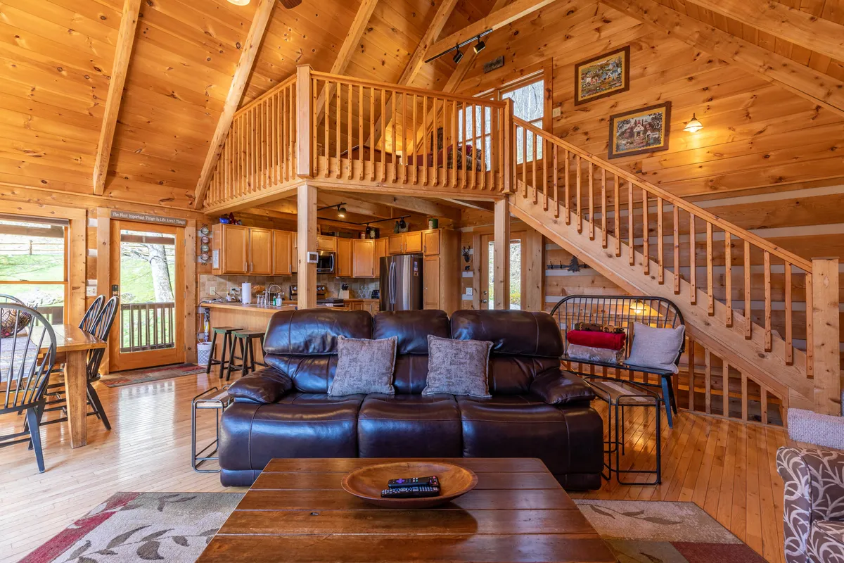 An inviting view of the main living space with a brown leather sofa, wooden staircase, kitchen area, and large windows. The layout encourages family gatherings and relaxation, with plenty of space for everyone.