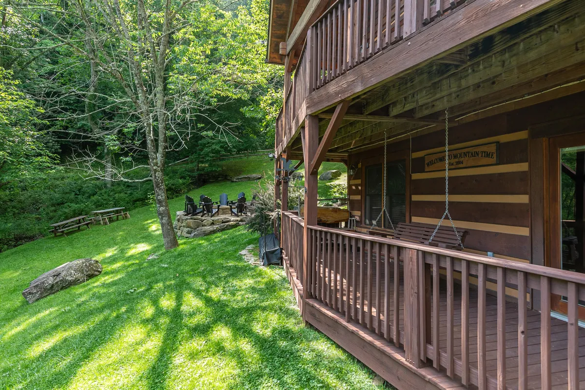 A peaceful view of the cabin’s exterior, with a green lawn, an outdoor seating area, and surrounding trees. There’s a visible fire pit for gathering, and the porch offers a spot for watching sunsets or enjoying nature.