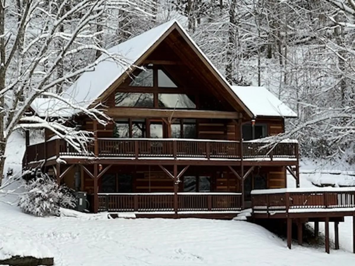 A striking A-frame cabin is nestled amidst a snow-covered landscape, its wooden deck partially blanketed in white. The scene captures the cozy charm of winter retreats, with the inviting deck promising space for stargazing or sipping cocoa after a day on the slopes.