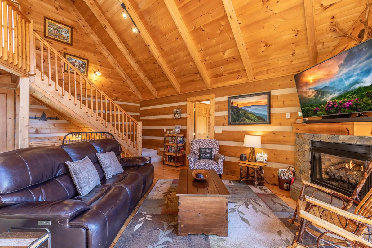 A cozy interior scene featuring a leather sofa facing a modern electric fireplace, with a TV and a wooden coffee table. A staircase leads to an open loft, while the inviting decor encourages relaxation and togetherness.