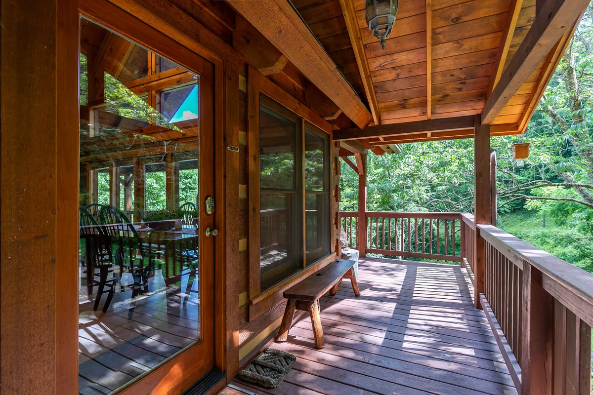 A charming wooden porch surrounded by lush greenery, with a glimpse of a dining table through the window. The porch invites guests to relax outdoors, connecting the home directly to nature—an ideal spot to unwind after a day of exploring with pets.