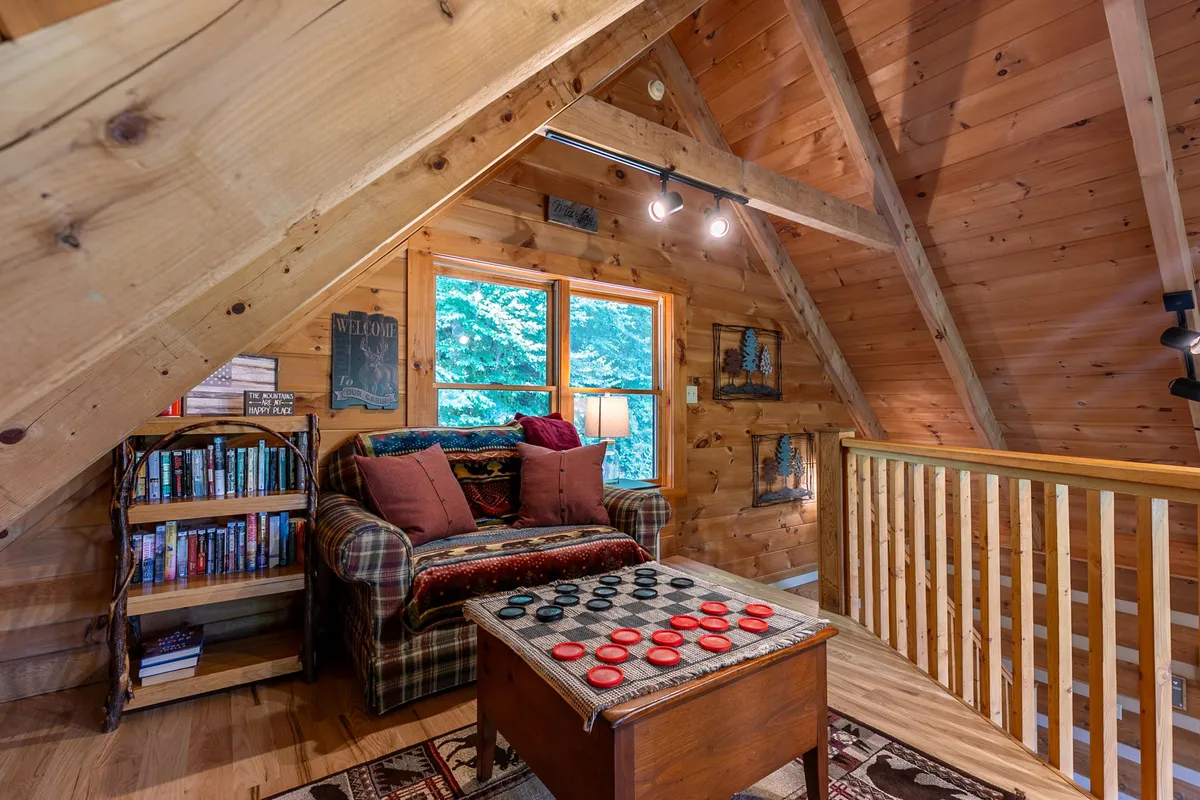 A relaxed seating area with a plaid couch, checkerboard table, bookshelf, and large windows overlooking the outdoors. The space invites quiet moments, board games, or reading with mountain vistas just outside.