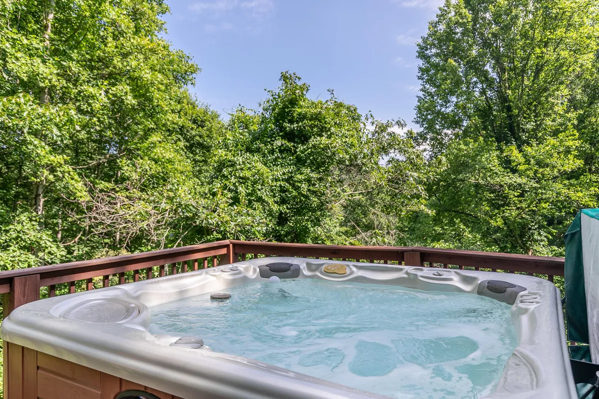 A private hot tub set on a wooden deck amidst lush greenery, with sturdy railings framing the view. The hot tub is perfect for relaxing while enjoying tranquil nature views or stargazing in the evening.