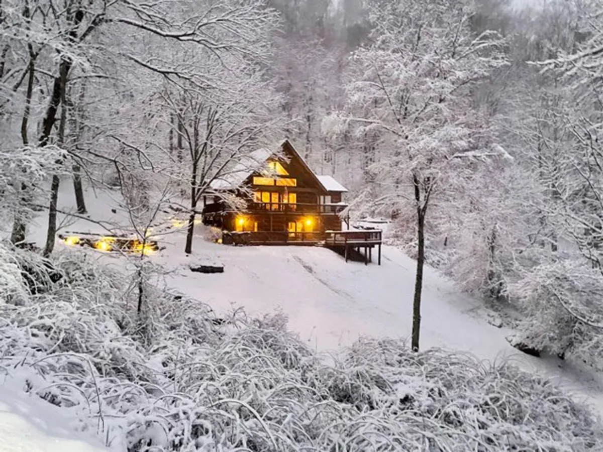 A warmly-lit house stands amidst a snow-covered landscape and frosted trees, exuding comfort and security even in winter. The inviting glow from within contrasts with the chilly outdoors, hinting at robust amenities and year-round accessibility.